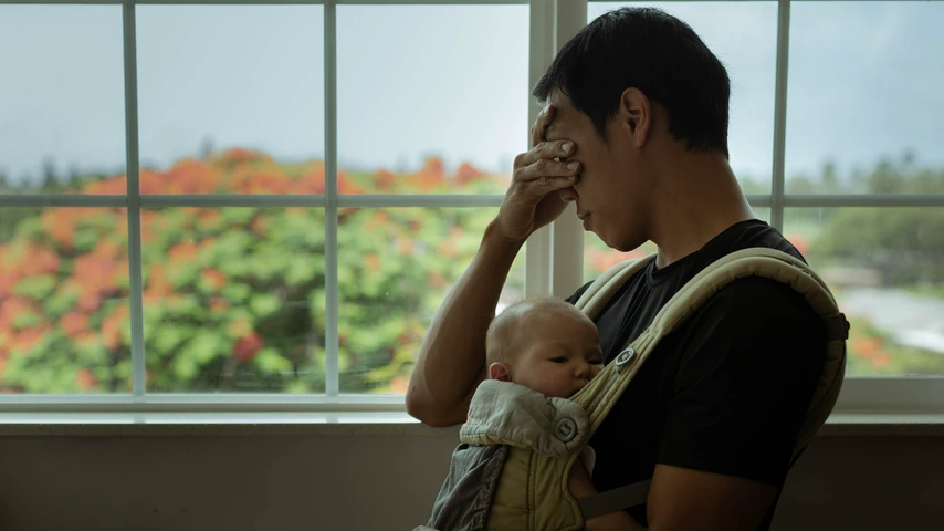 Upset father carrying baby in a sling on his chest